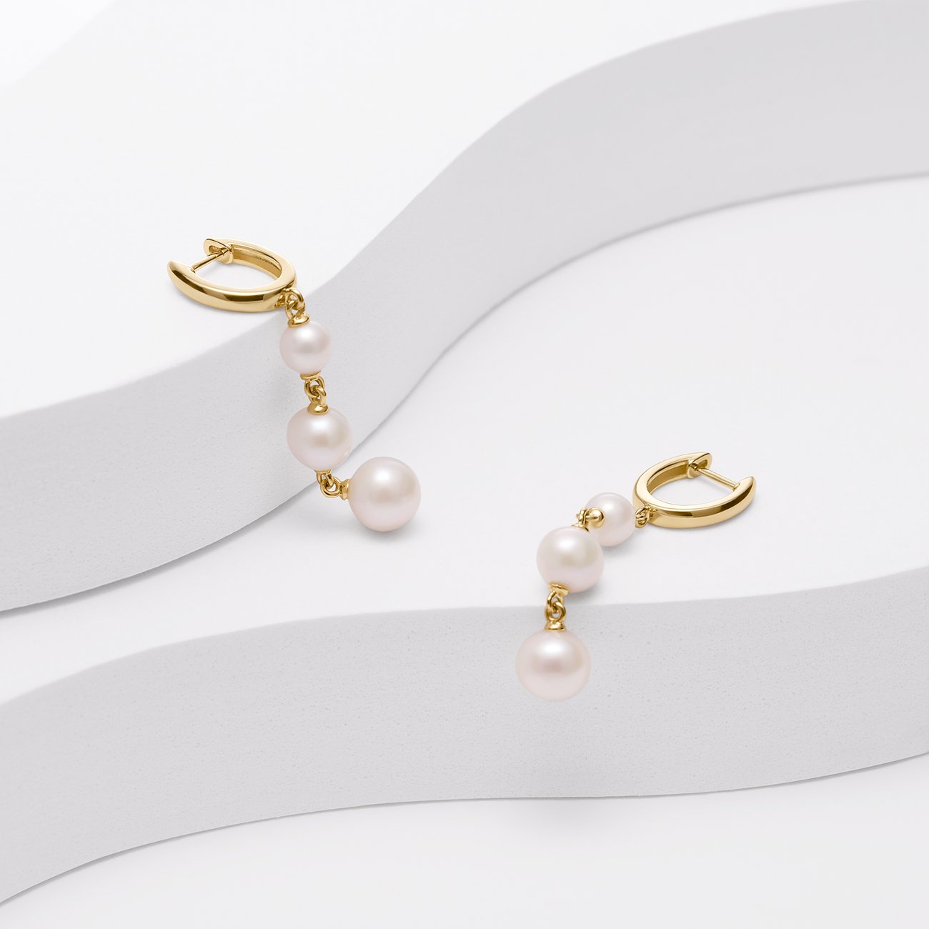 Två gyllene YAMOKO örhängen i 585 gult guld, vardera med tre vita pärlor i fallande storlek.