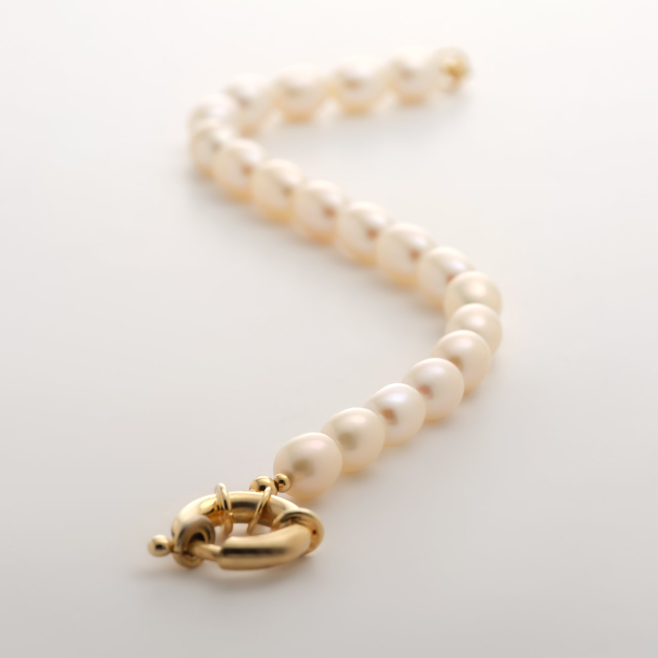 Bracelet YAMOKO en or jaune 585 avec perles ovales, à plat sur fond blanc, fermoir net.