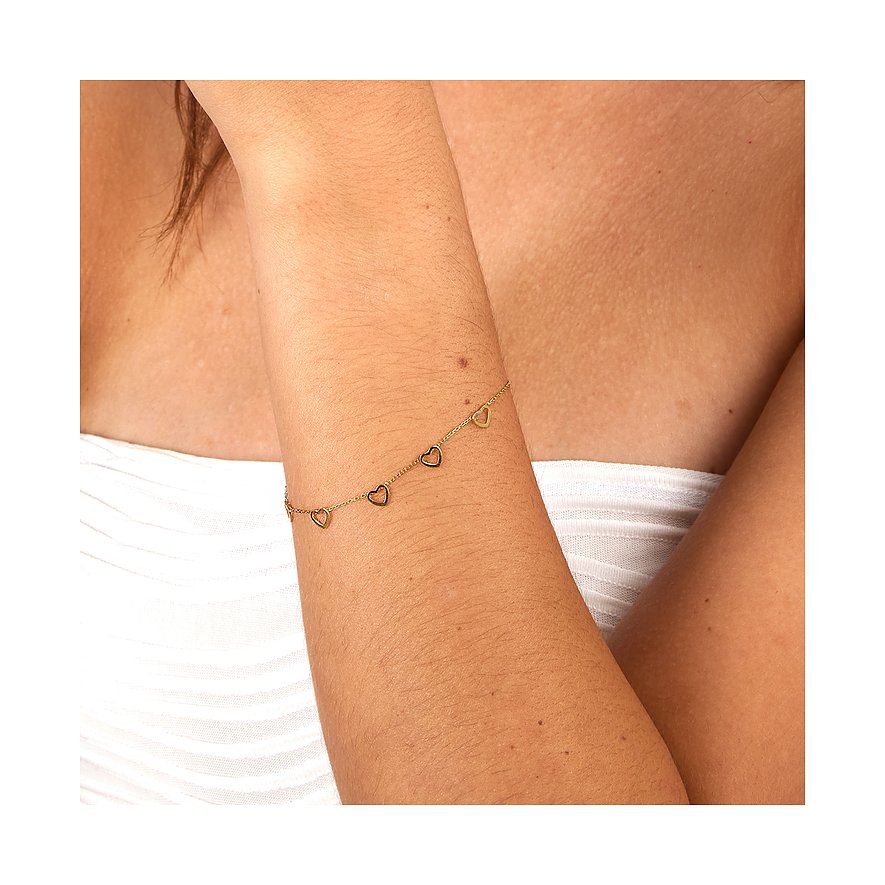 Bijou de bras en or jaune 585 CHRIST avec motif cœur sur un bras sur fond couleur peau et beige.