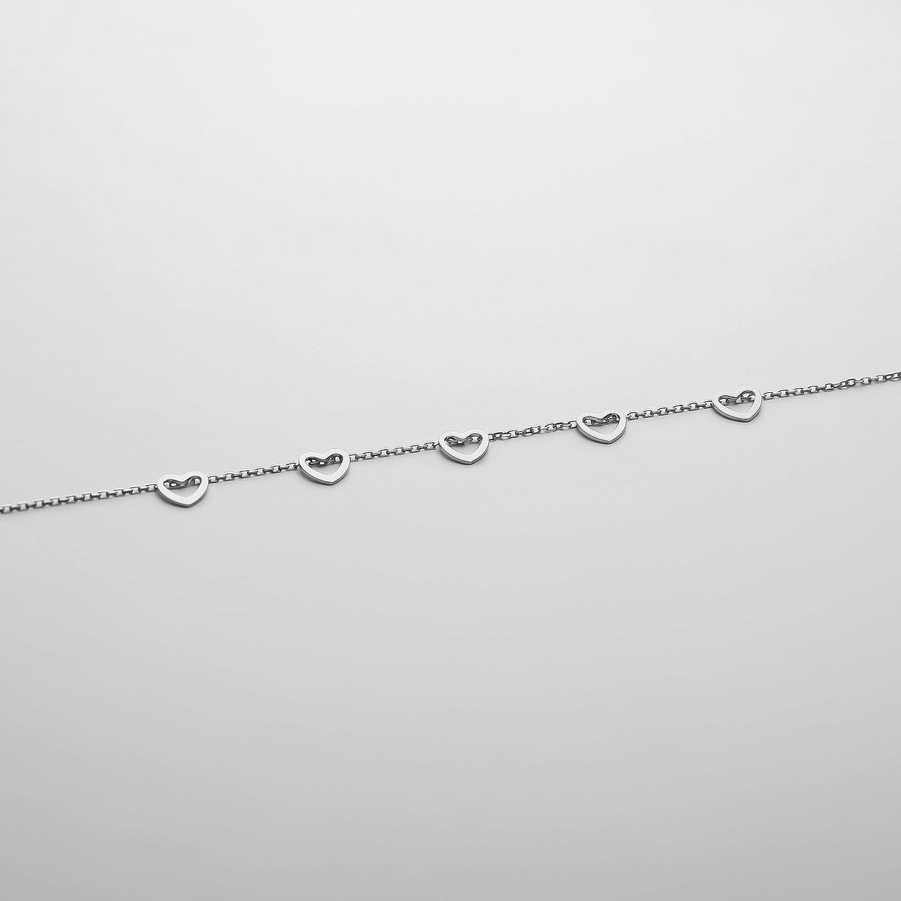 CHRIST 585er Weißgold Armschmuck mit mehreren kleinen Herzanhängern, liegend vor weißem Hintergrund.