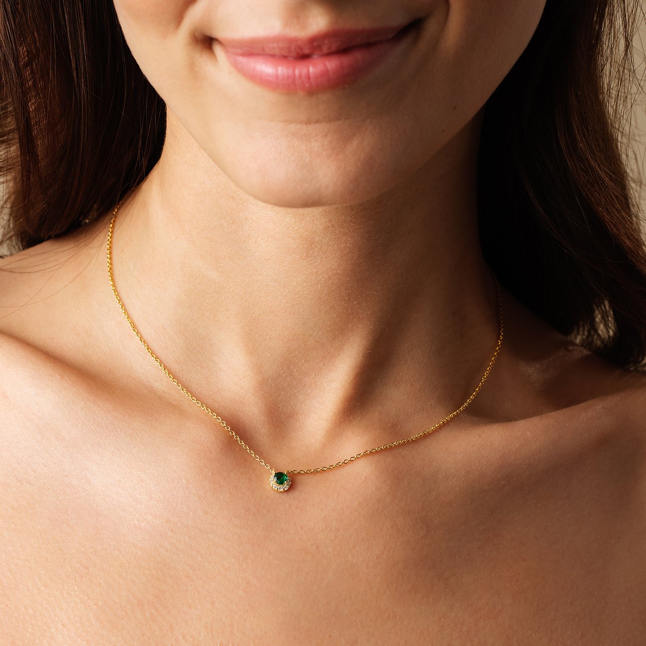 En kvinna bär ett FAVS halsband i guldpläterat 925 sterlingsilver med en rund grön zirkoniasten.