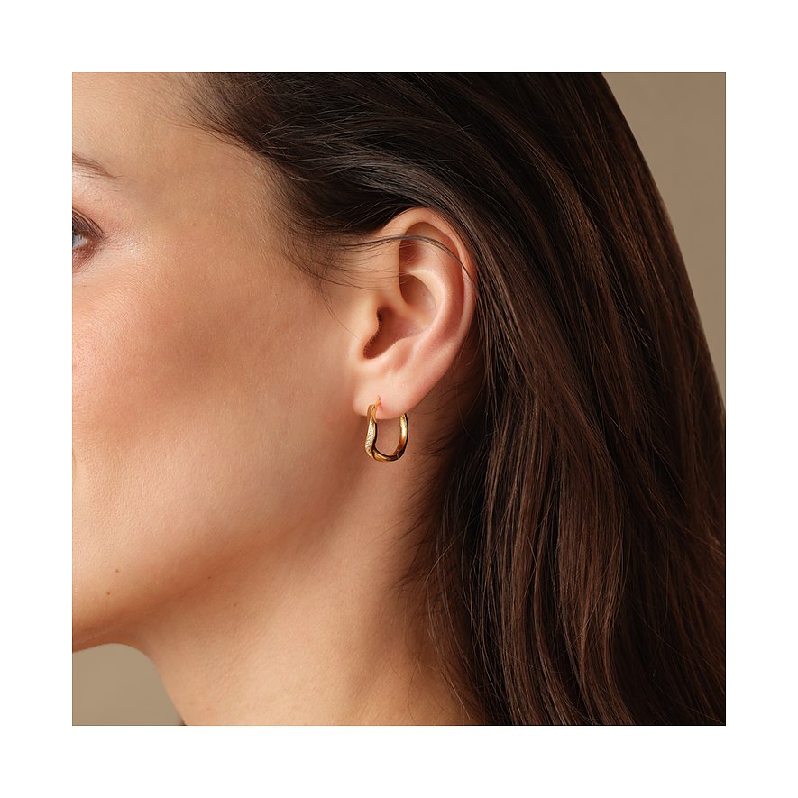 Une boucle d'oreille circulaire FAVS en argent sterling 925 doré sur une oreille. Les cheveux sont foncés.