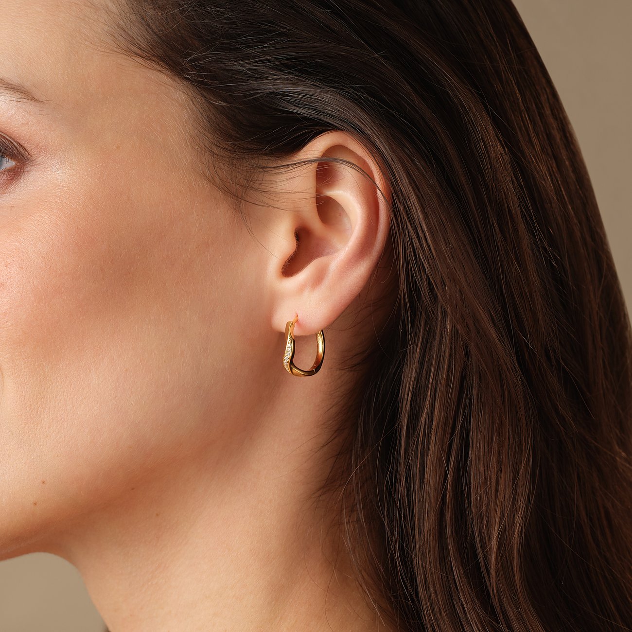 Une boucle d'oreille circulaire FAVS en argent sterling 925 doré sur une oreille. Les cheveux sont foncés.