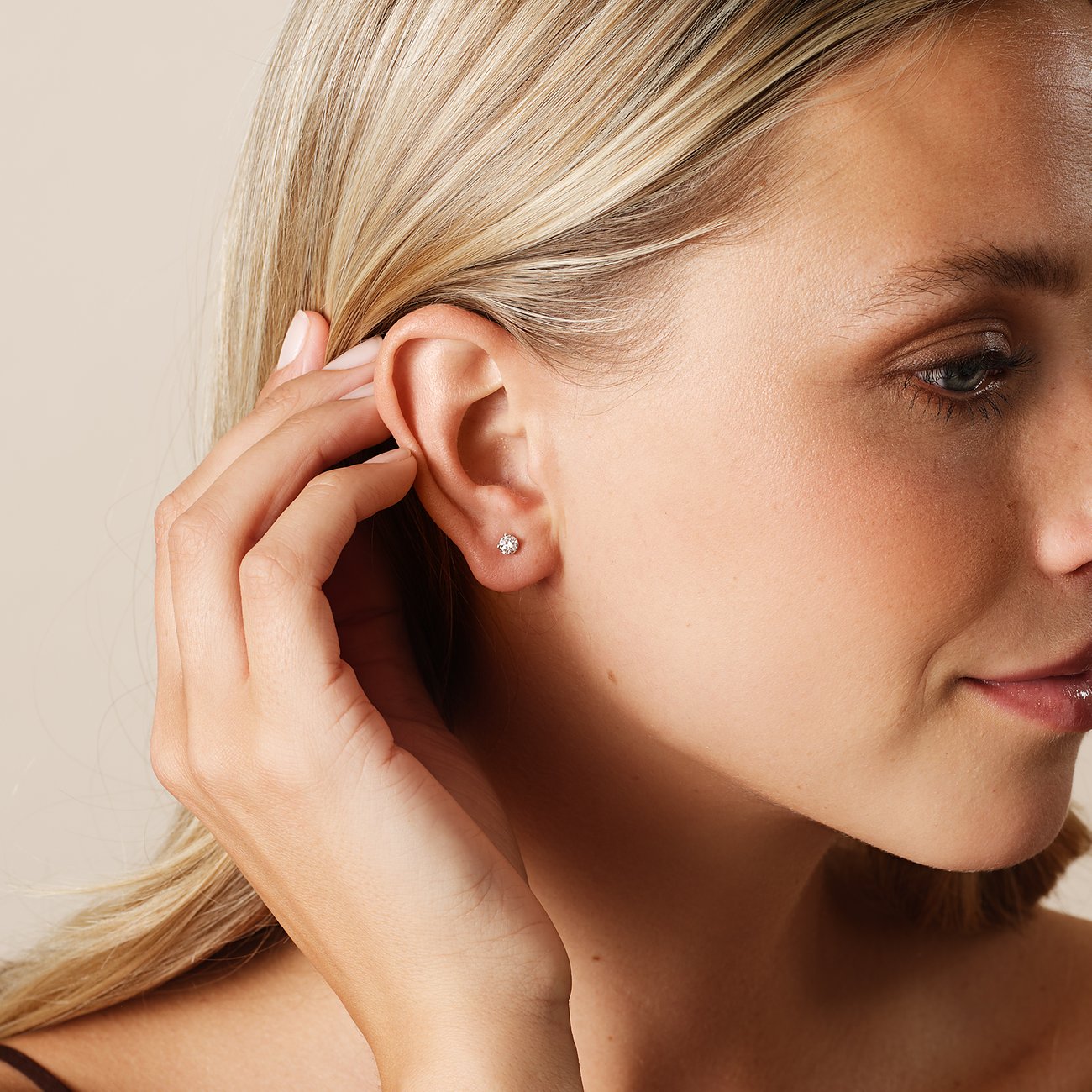 Ein blondes Model trägt einen kleinen Ohrstecker von CHRIST aus Weißgold mit einem Diamanten im Ohr.