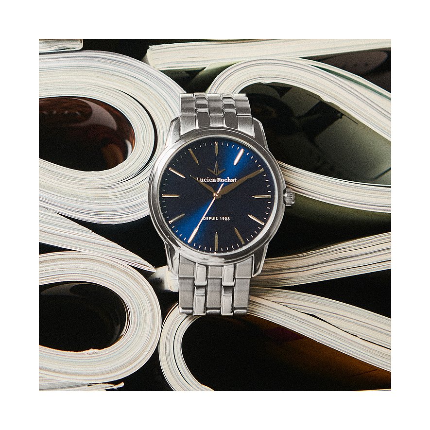 Une montre ronde Lucien Rochat pour homme en acier inoxydable avec cadran bleu, posée sur des magazines roulés.