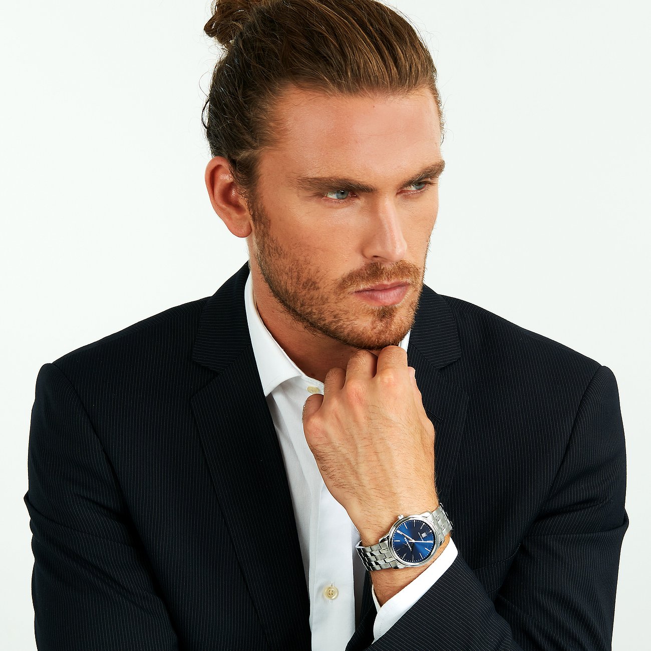 Un homme aux cheveux attachés porte une montre homme Lucien Rochat en acier inoxydable à cadran bleu.
