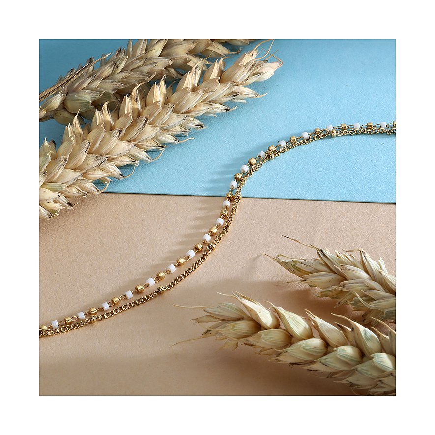 La Petite Story Armschmuck aus gelb-goldenem Edelstahl und weißer Emaille auf beigem und blauem Hintergrund.
