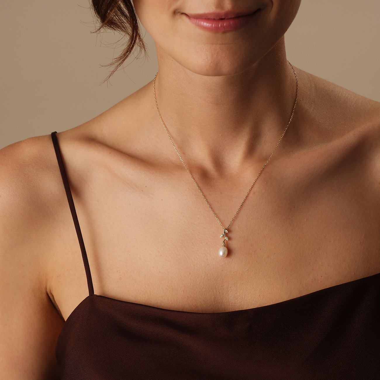Eine Frau trägt eine CHRIST Perlenkette aus 585 Gelbgold mit einem Perlenanhänger auf braunem Satinstoff.