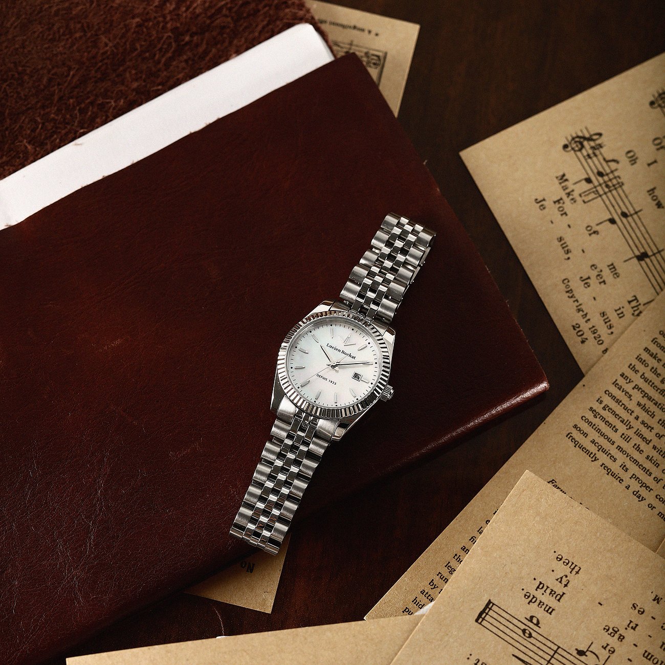 Eine Lucien Rochat Damenuhr aus Edelstahl mit einem weißen Zifferblatt liegt auf einem braunen Notizbuch.