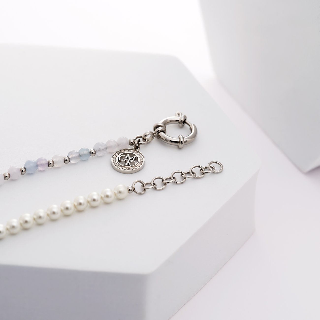 Gros plan d'un bracelet Guido Maria Kretschmer en acier inoxydable, brins de cristaux colorés et perles sur fond blanc.