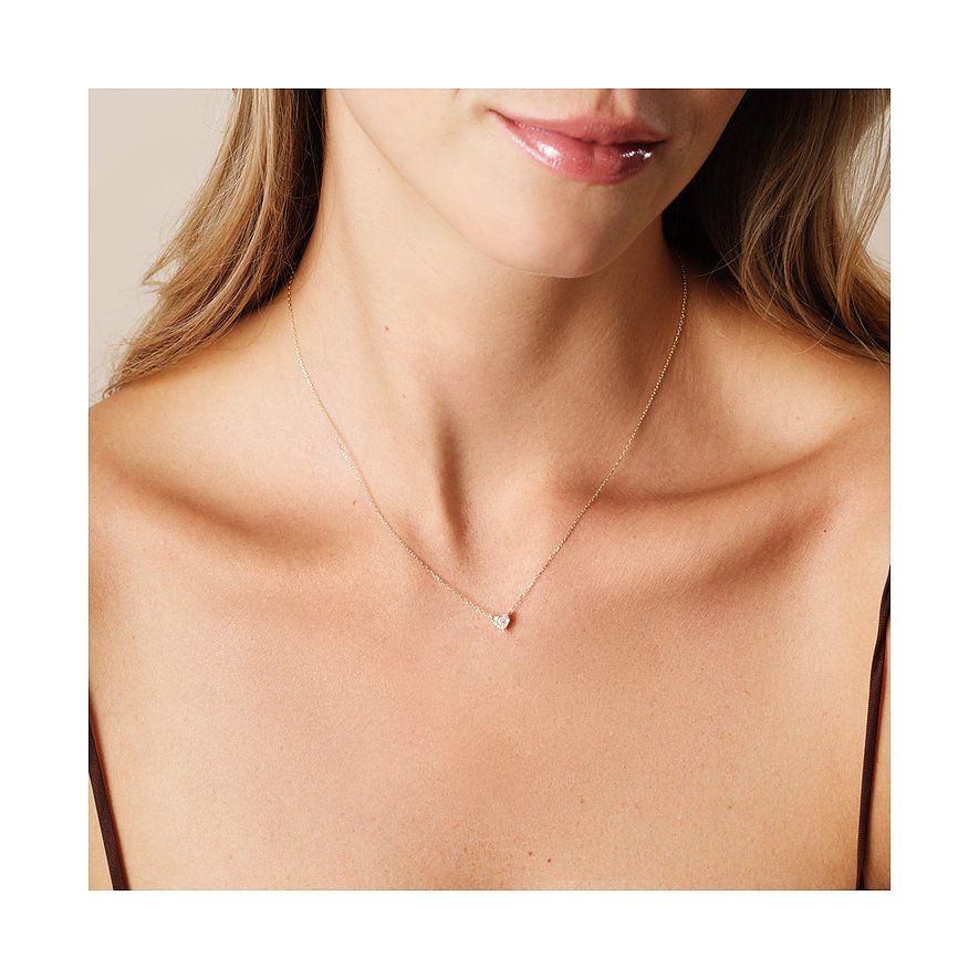 Eine Frau trägt eine CHRIST Herzkette aus 585 Gelbgold mit einem kleinen Diamanten in Herzform auf der Brust.