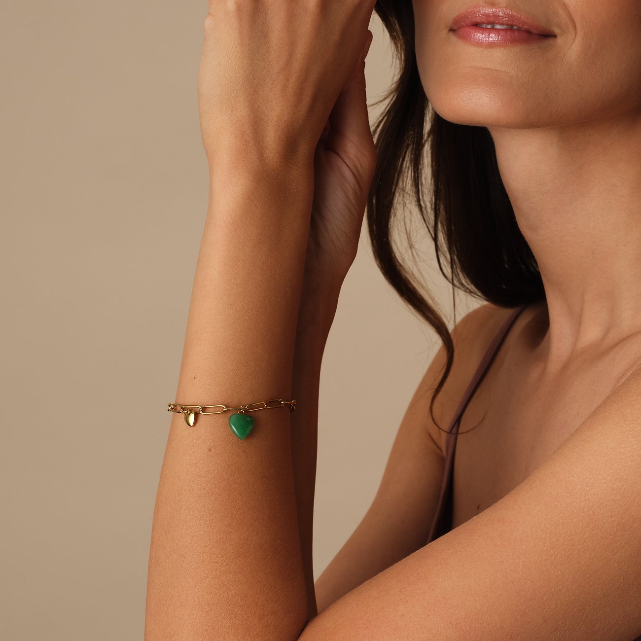 Bracelet doré en acier inoxydable Guido Maria Kretschmer, cristal vert en forme de cœur, au bras d'une femme.