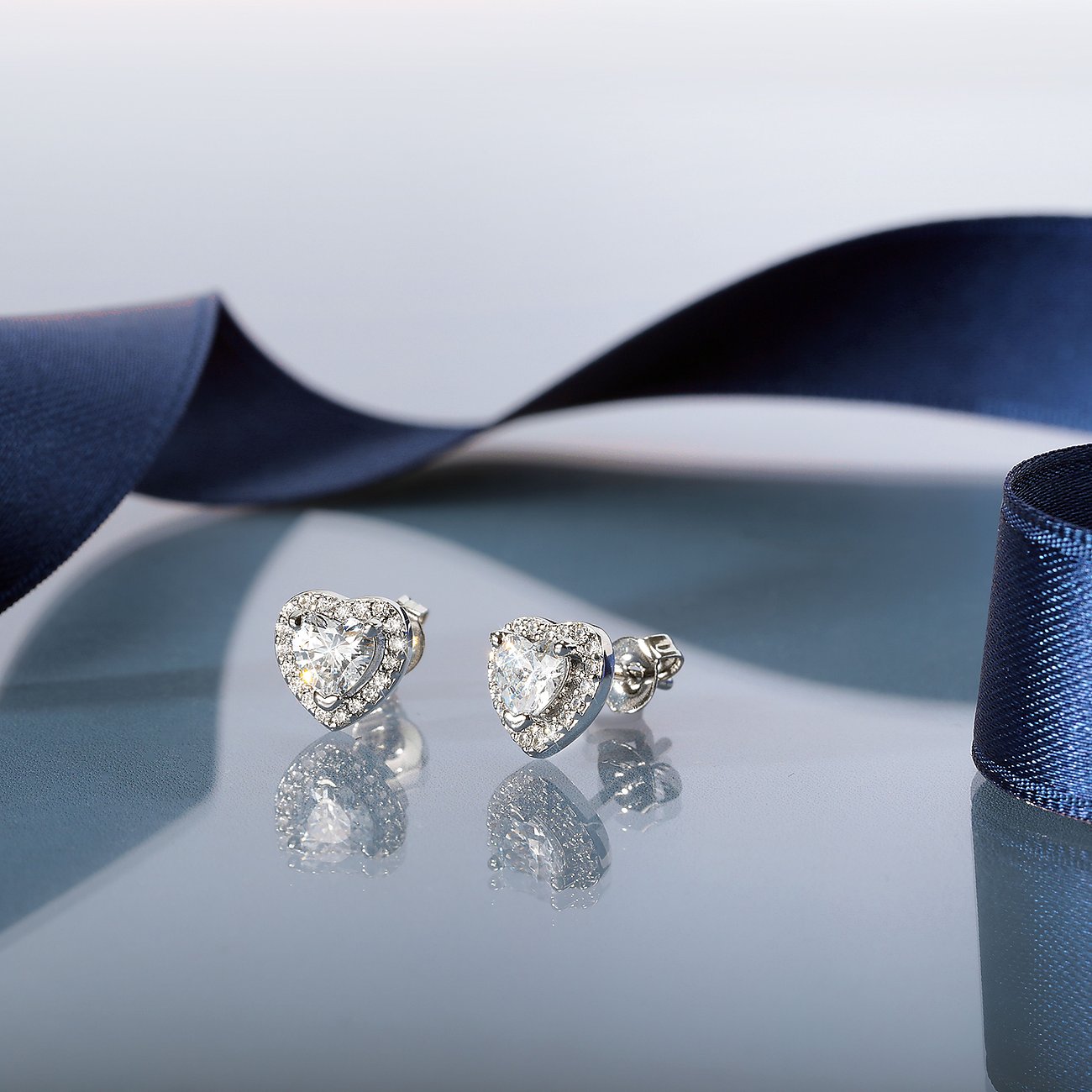 Puces d'oreilles Morellato en zircone cœur, argent recyclé, petites pierres autour de la pierre centrale, sur ruban bleu.