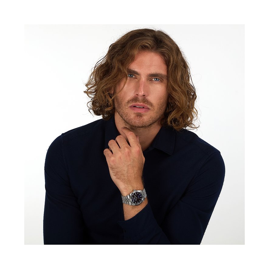 Ein Mann mit lockigem Haar trägt eine Lucien Rochat Herrenuhr aus Edelstahl am linken Handgelenk.
