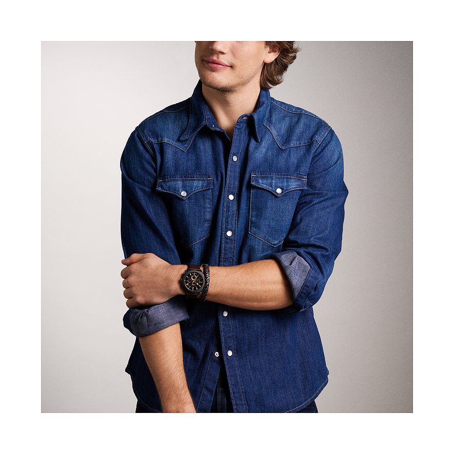 Ein Mann im Denim-Hemd trägt ein Fossil-Uhren-Set aus Edelstahl am Handgelenk