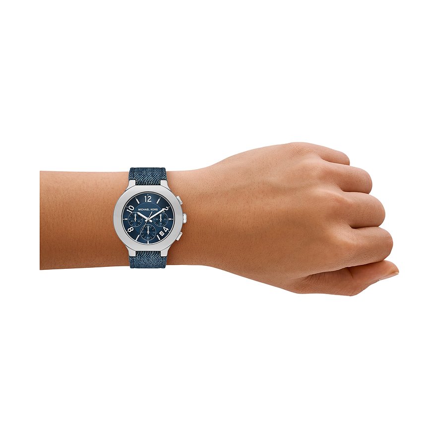 Eine Michael Kors Damenuhr aus Edelstahl mit blauem Zifferblatt und blauem Denimarmband, am Handgelenk getragen.