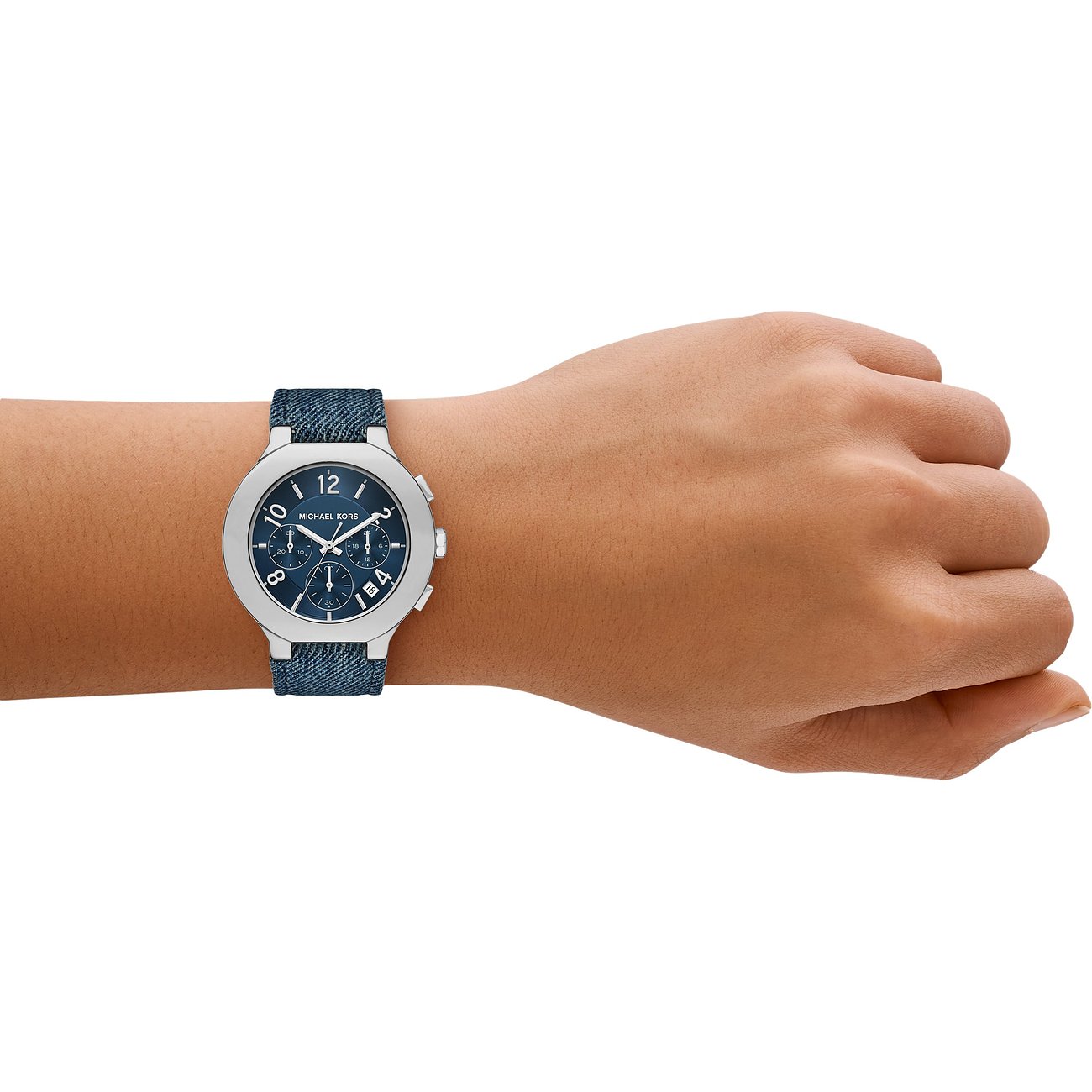 Eine Michael Kors Damenuhr aus Edelstahl mit blauem Zifferblatt und blauem Denimarmband, am Handgelenk getragen.