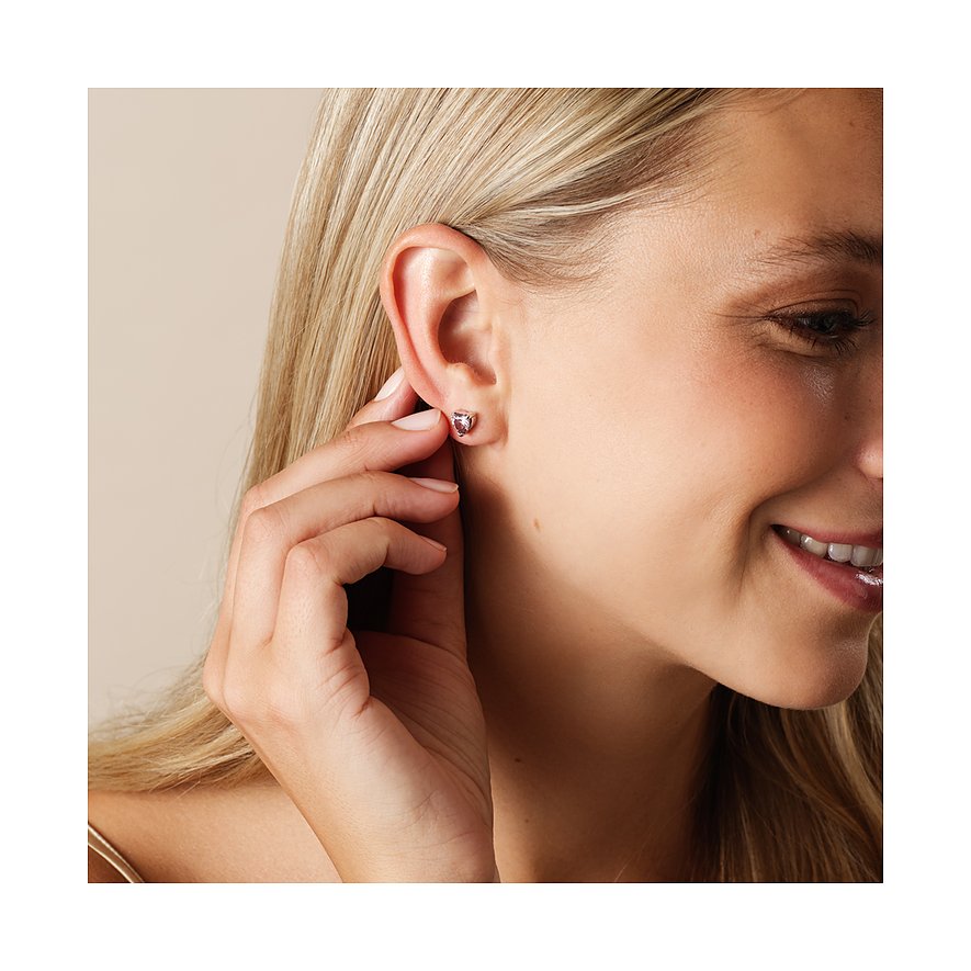 Eine Frau trägt einen CHRIST Ohrstecker aus recyceltem 925er Silber mit herzförmigem Zirkonia-Farbstein in Purpurrot.