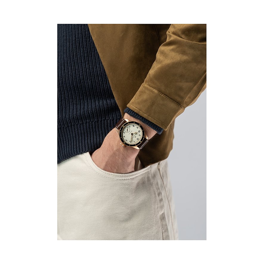 Am Handgelenk eines Mannes Hamilton Herrenuhr aus Bronze mit braunem Lederarmband und cremefarbenem Zifferblatt.