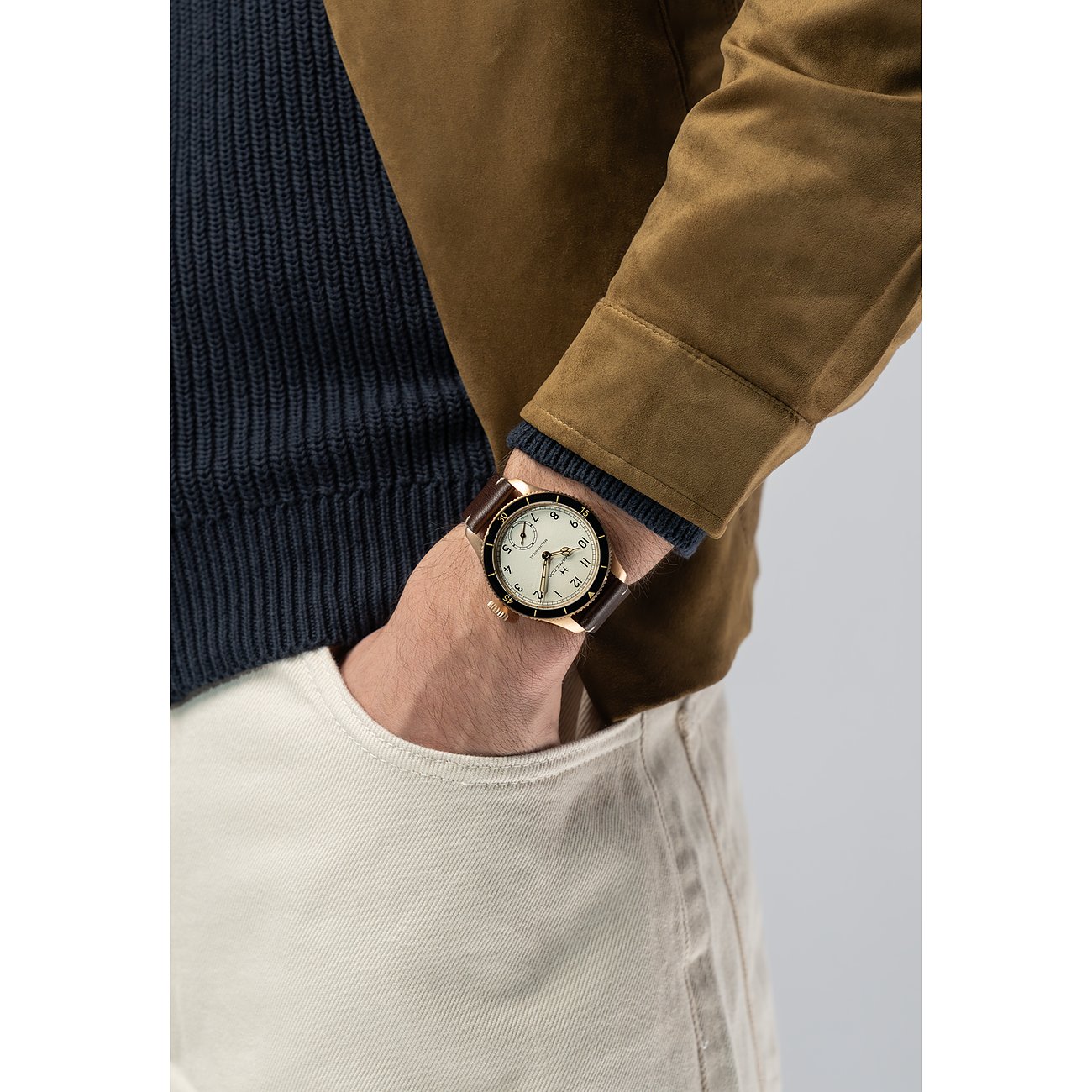 Am Handgelenk eines Mannes Hamilton Herrenuhr aus Bronze mit braunem Lederarmband und cremefarbenem Zifferblatt.