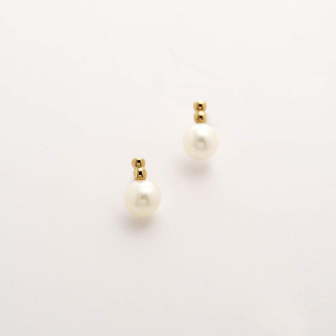 CHRIST öronsmycken i 375 gult guld med pärlor som diskreta örhängen, på vit bakgrund.