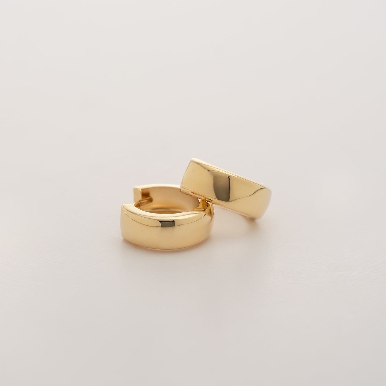 CHRIST Ohrschmuck aus 585 Gelbgold, zwei goldene Creolen, die schräg nebeneinander auf einer weißen Oberfläche liegen.