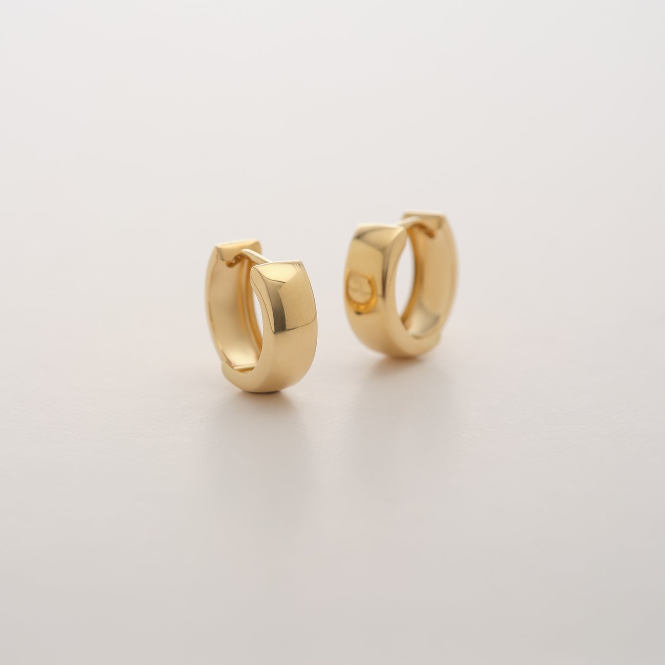 Ein Paar CHRIST Creolen aus 585 Gelbgold im Mini-Format liegen leicht schräg auf einer hellen Oberfläche.