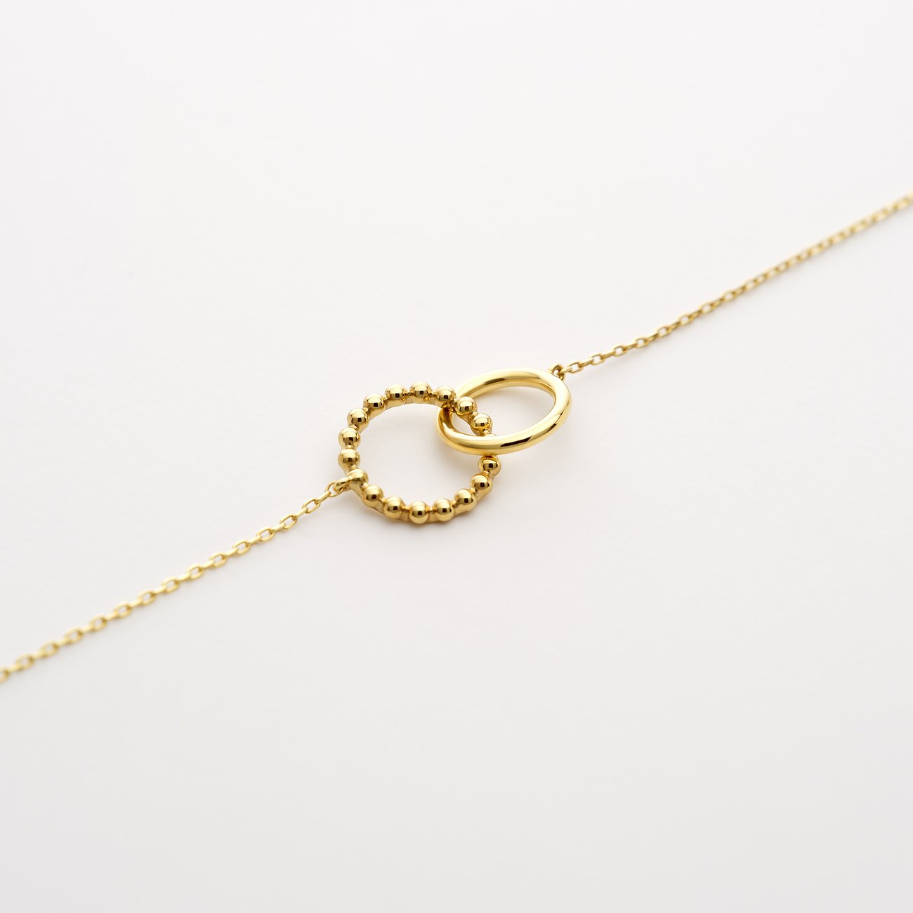 CHRIST armband i 585 gult guld med två sammanflätade ringar, varav den ena är prydd med små kulor.