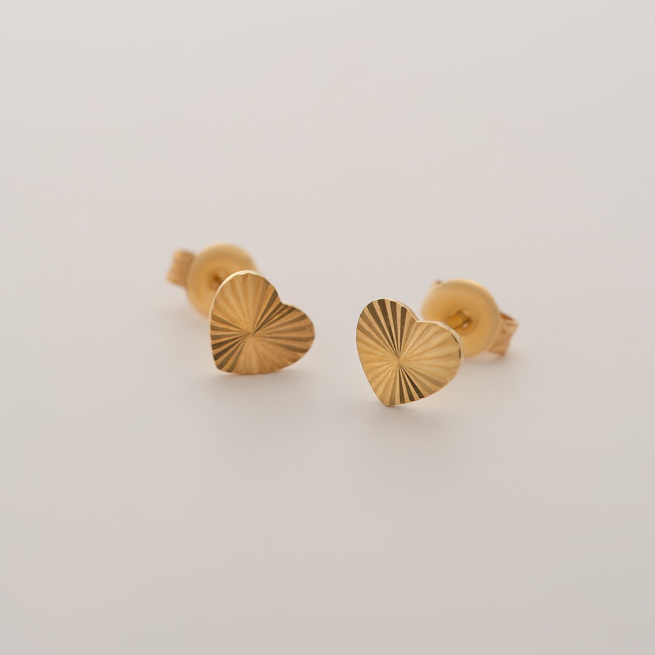CHRIST Ohrstecker aus 375er Gelbgold, geformt als Herzen mit radialer Riffelung, von vorne dargestellt.