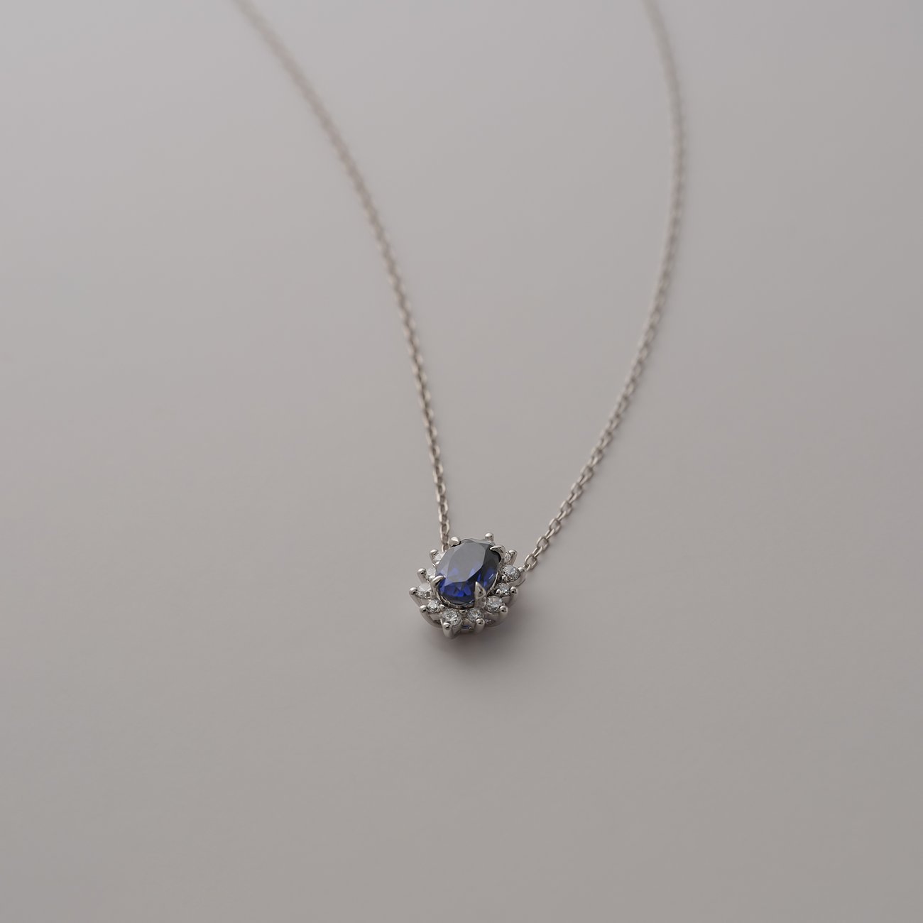 Collier CHRIST en or blanc 585 avec saphir ovale comme pierre de couleur, entouré de pierres taillées.