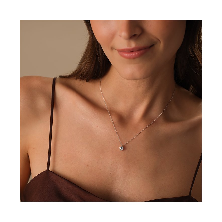 Eine Frau trägt eine CHRIST Weißgoldkette mit einem einzelnen runden Diamanten, der auf ihrem Dekolleté funkelt.