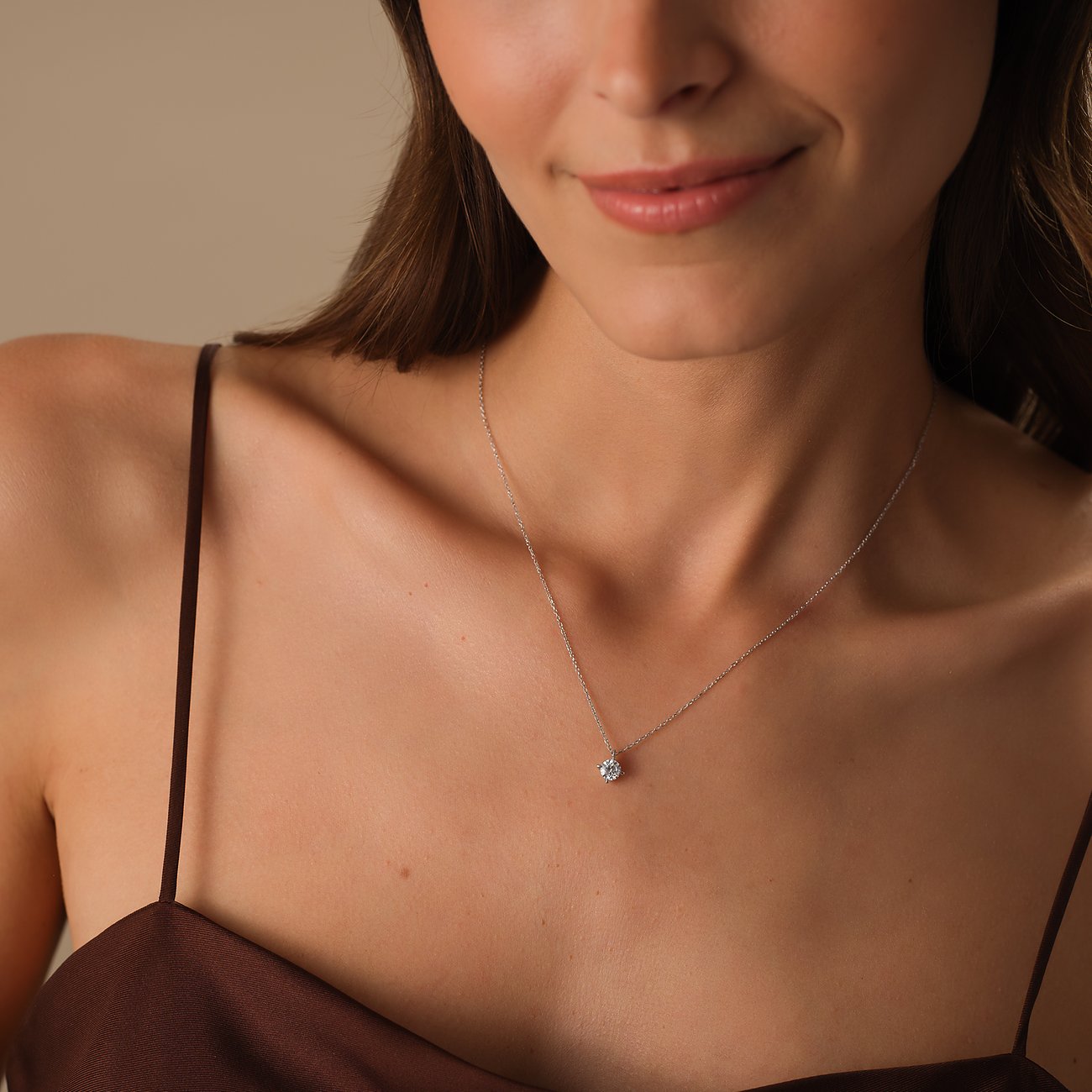 Eine Frau trägt eine CHRIST Weißgoldkette mit einem einzelnen runden Diamanten, der auf ihrem Dekolleté funkelt.