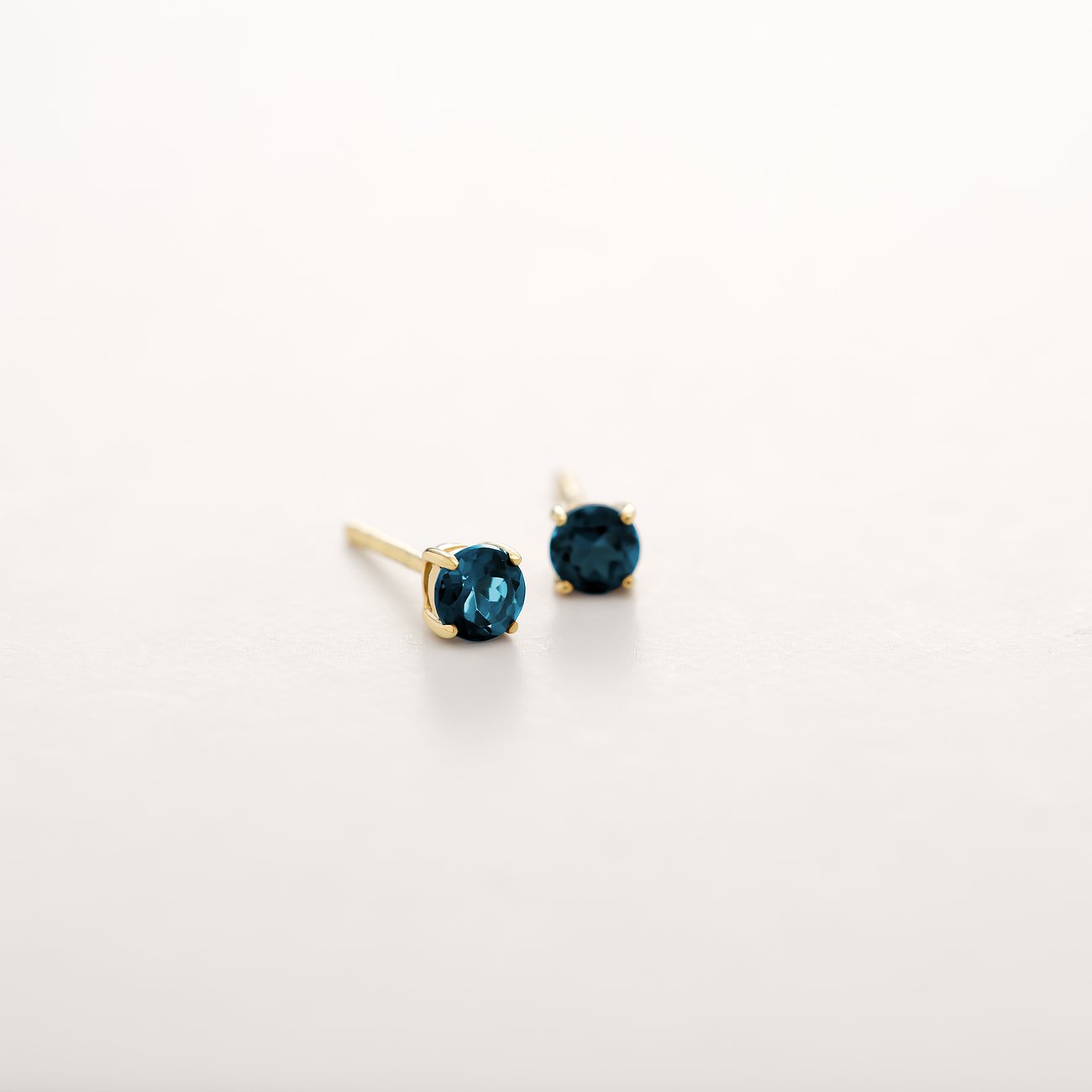 CHRIST Ohrstecker aus 375er Gelbgold mit facettiertem blauem Topas als Blickfang auf reinweißem Grund.