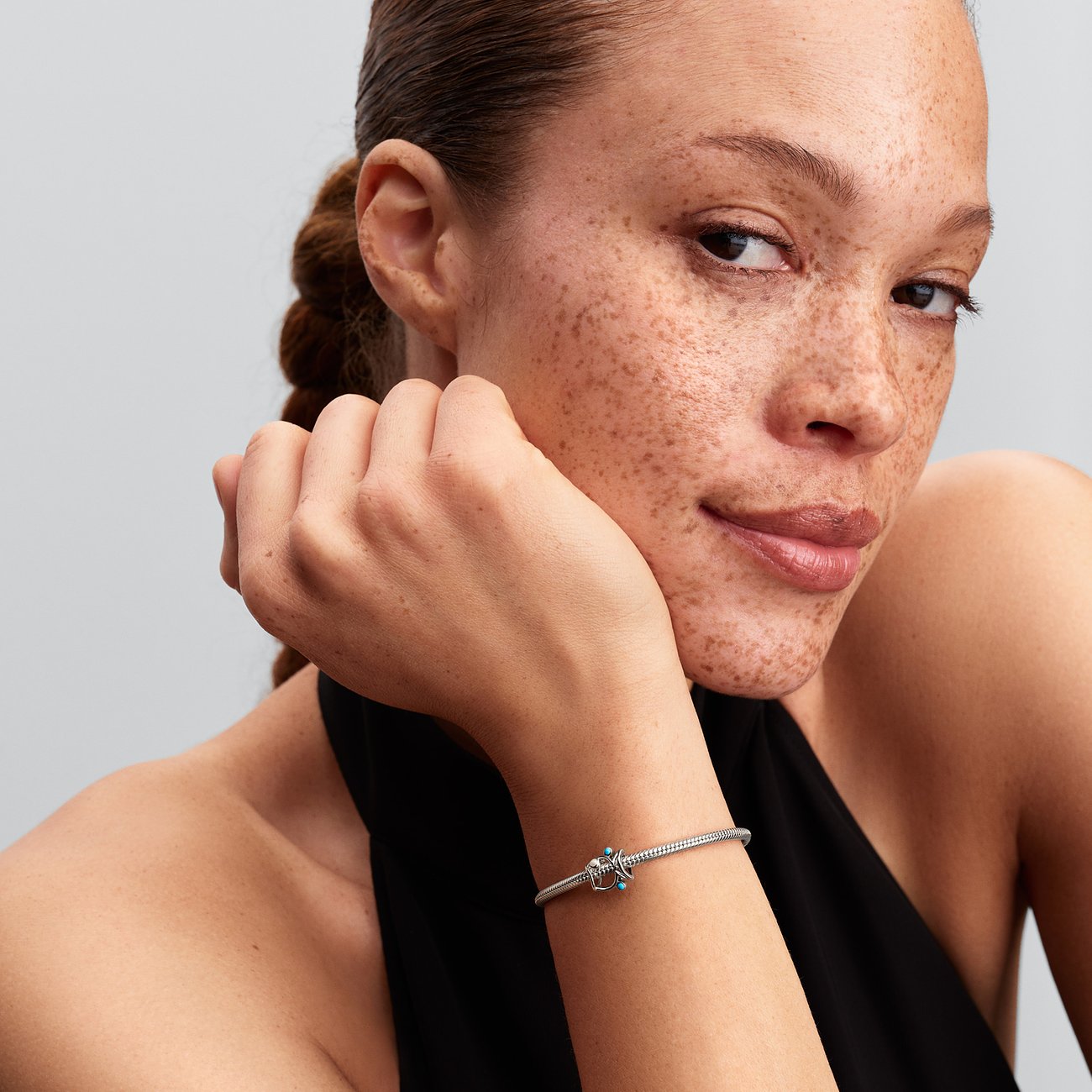 Nahaufnahme einer Frau mit Sommersprossen, ihr Arm ruht auf dem Kinn, ein silbernes Pandora Armband ziert ihr Handgelenk