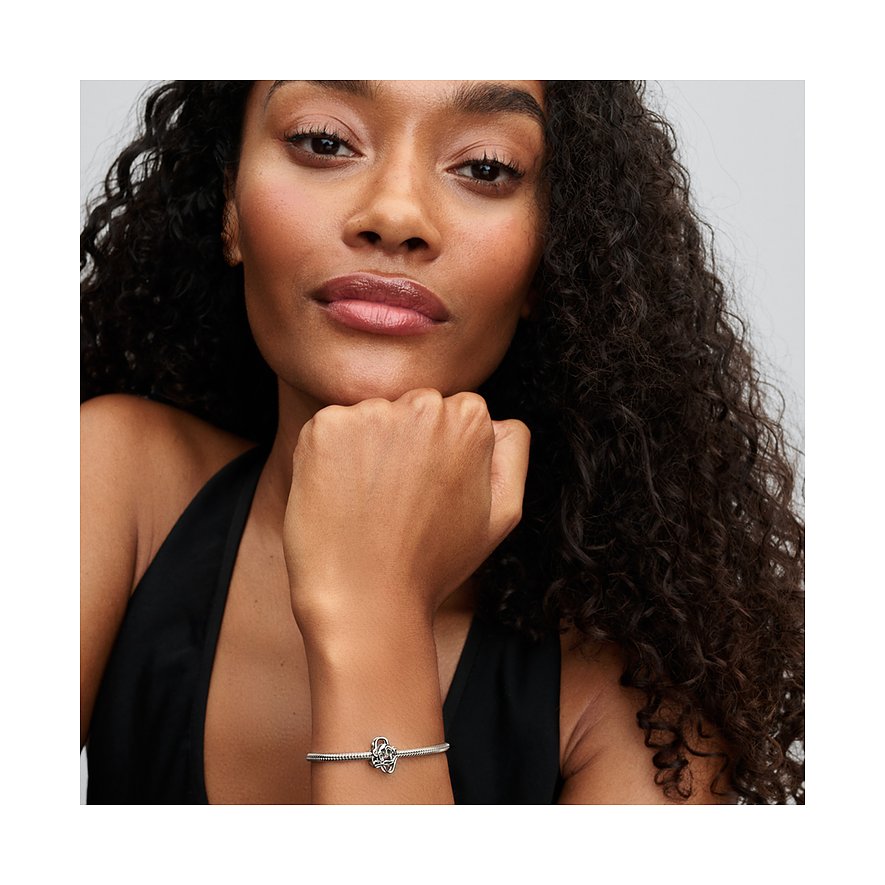 Nahaufnahme einer Frau mit lockigem Haar, die ein silbernes Pandora Armband mit einem Anhänger am Handgelenk trägt.