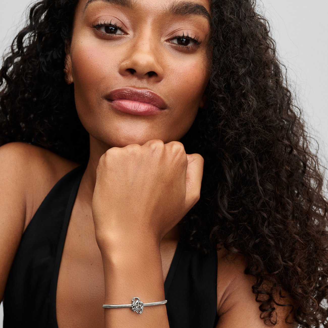 Nahaufnahme einer Frau mit lockigem Haar, die ein silbernes Pandora Armband mit einem Anhänger am Handgelenk trägt.
