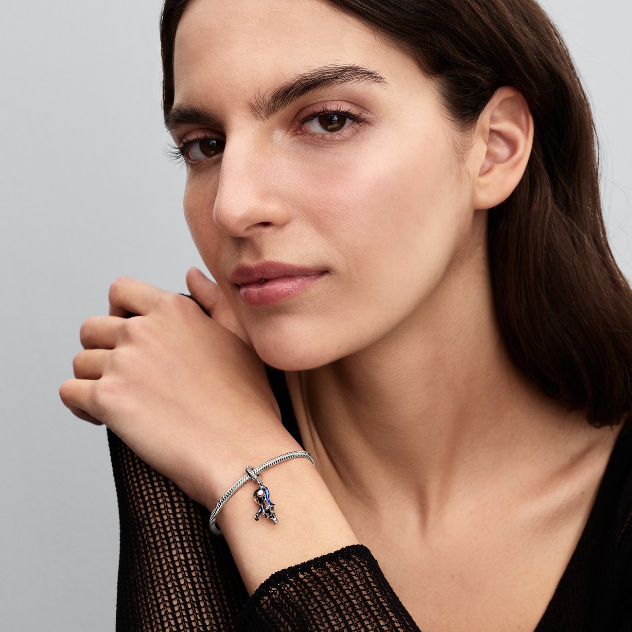 Nahaufnahme einer Frau, die ein Pandora Charm-Armband aus 925er Silber mit einem verspielten Emaille-Anhänger trägt.