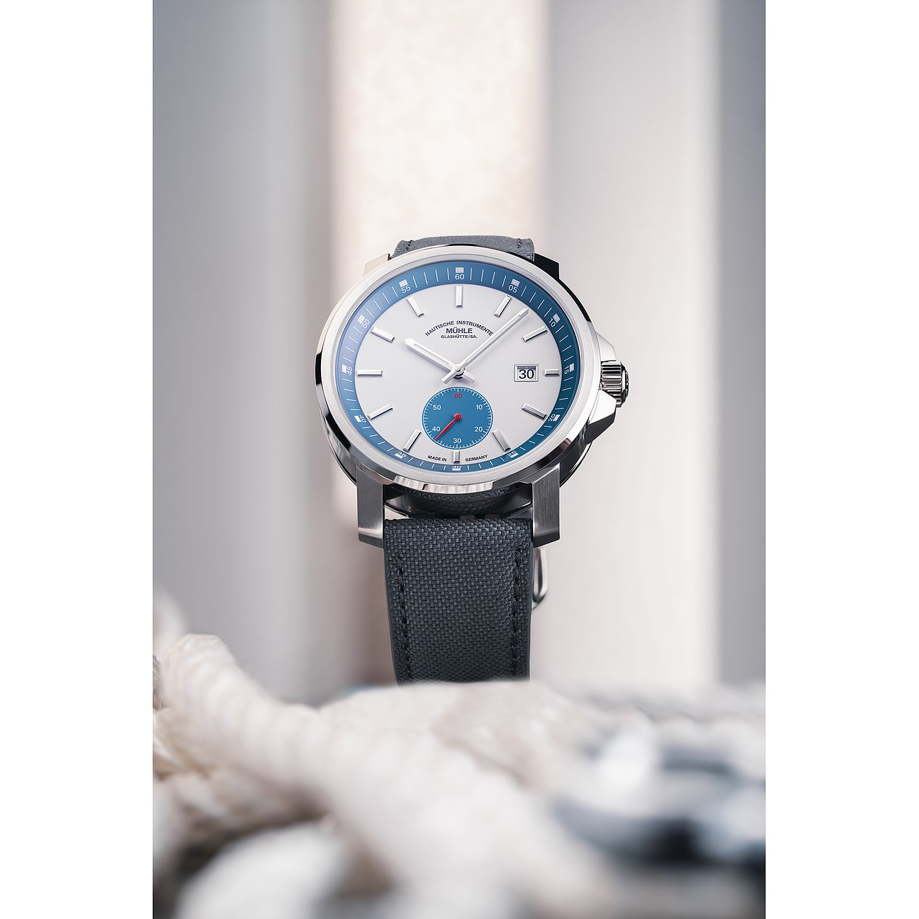 Mühle-Glashütte Herrenuhr mit Edelstahlgehäuse, weißem Zifferblatt und blauem Ring.