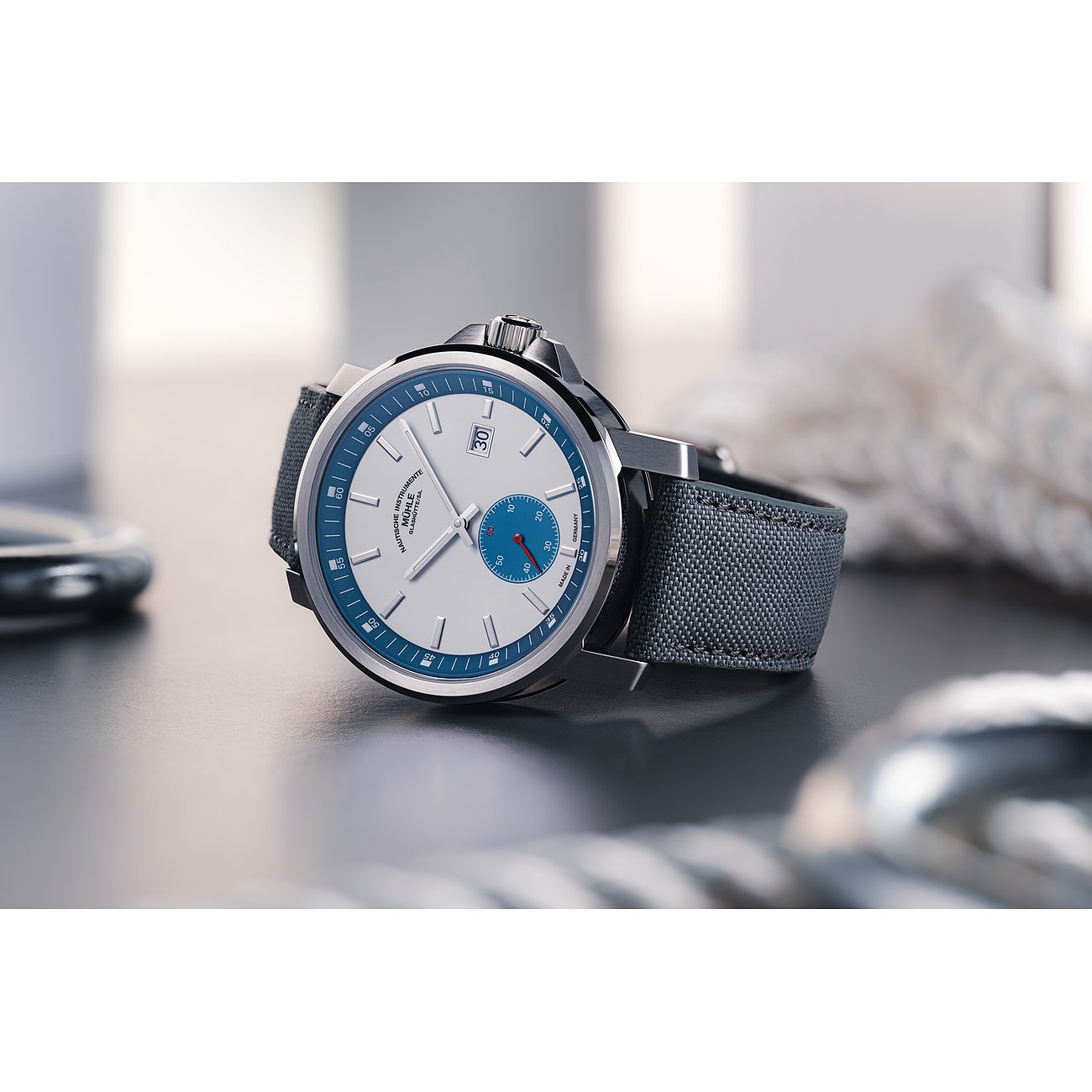 Mühle-Glashütte Herrenuhr mit Edelstahlgehäuse, weißem Zifferblatt und blauer Lünette.