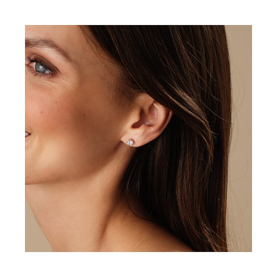 Nahaufnahme einer lächelnden Frau, die einen CHRIST Ohrstecker aus 585er Weißgold mit funkelnden Diamanten trägt.