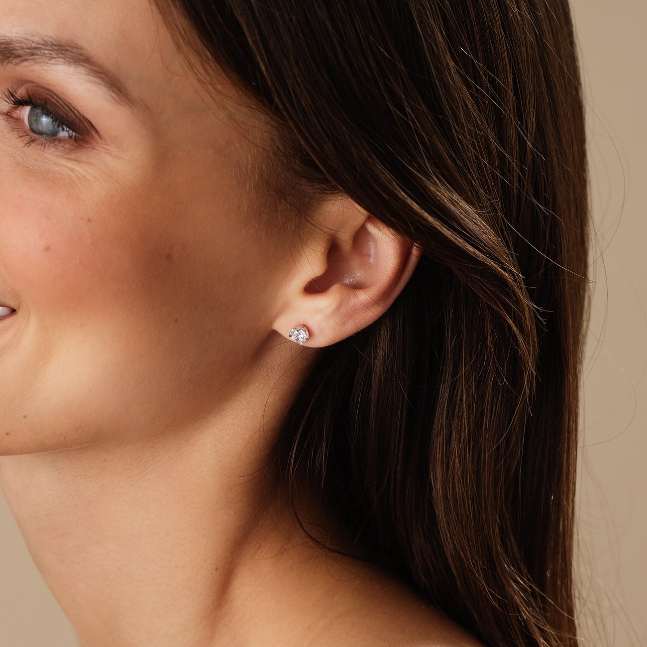 Nahaufnahme einer lächelnden Frau, die einen CHRIST Ohrstecker aus 585er Weißgold mit funkelnden Diamanten trägt.