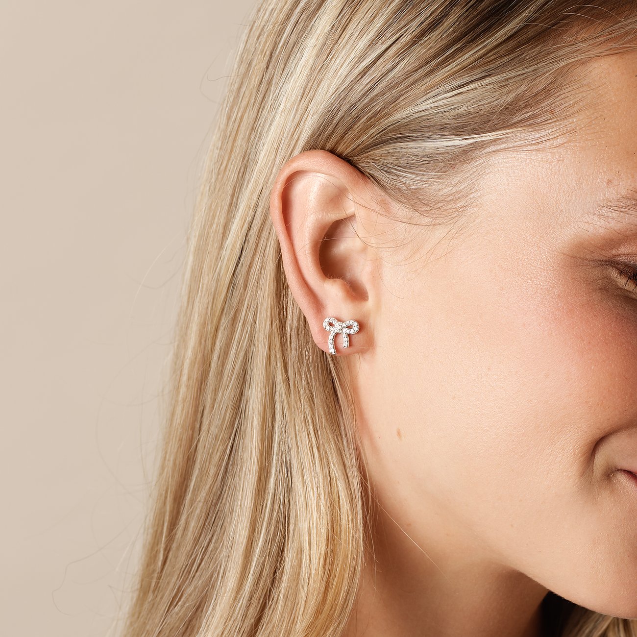 Ein CHRIST Schleifchen-Ohrstecker aus recyceltem Silber mit Zirkonia-Verzierung, getragen an einem Ohr.