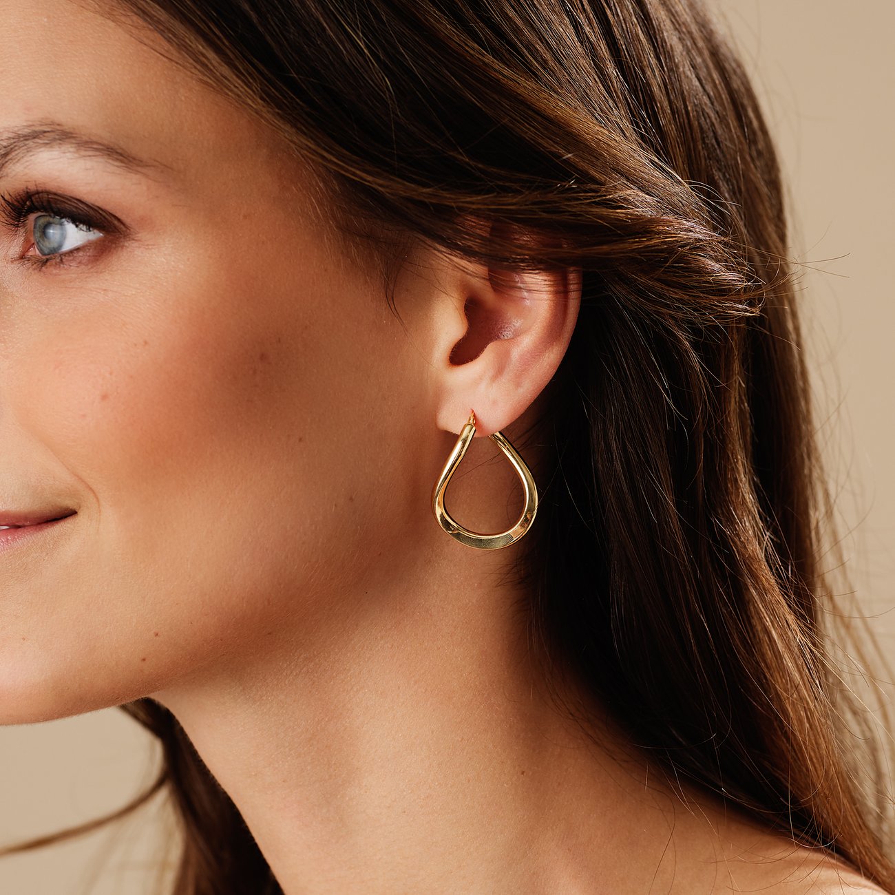 Nahaufnahme einer Frau, die am Ohr einen CHRIST Ohrring aus Gelbgold 585 trägt. Der Ohrring ist Tropfen-förmig.