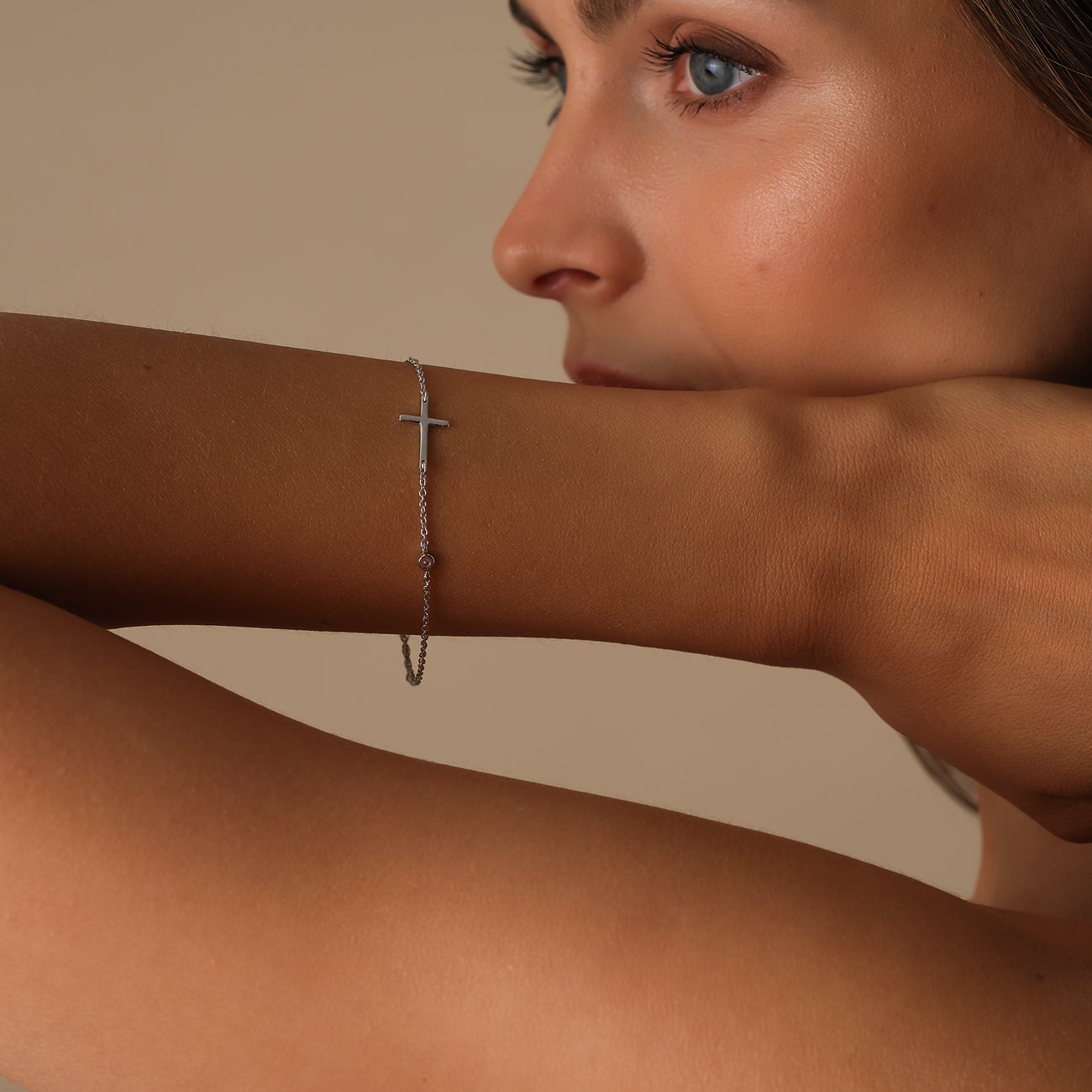 Ein zartes silbernes CHRIST Armband aus recyceltem Silber mit Kreuzanhänger und Zirkonia am Handgelenk eines Models.