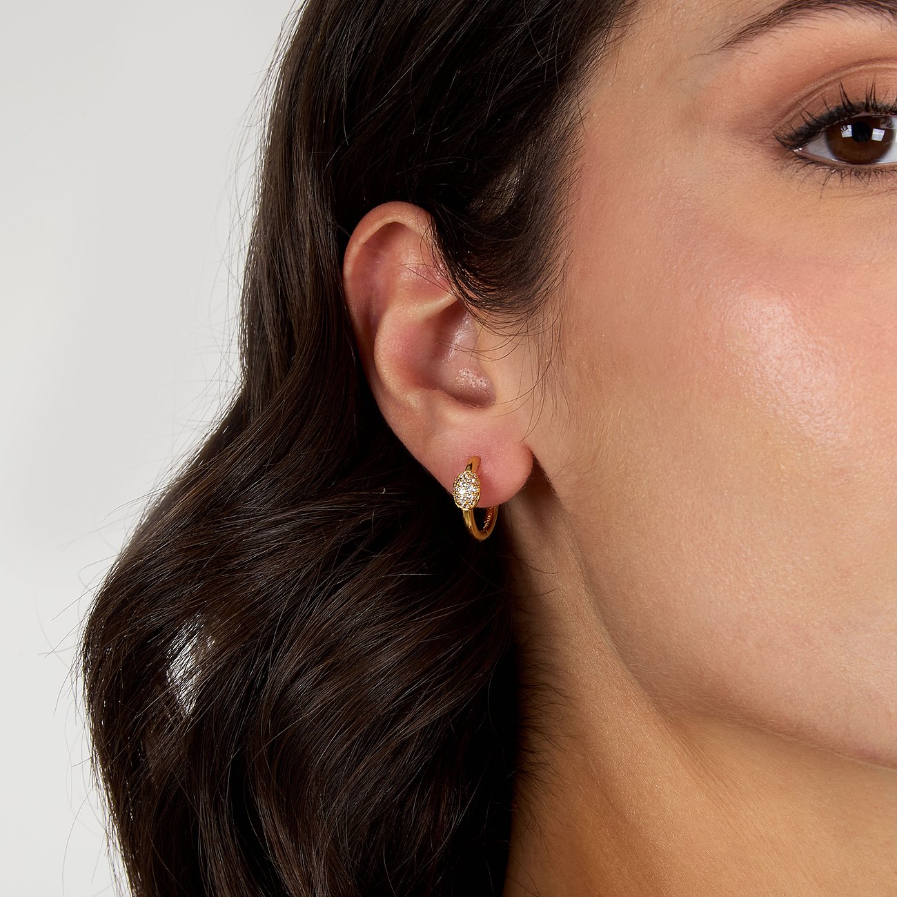 En kvinna bär ett litet, gyllene Morellato creolörhänge av återvunnet silver med gnistrande zirkonstenar.