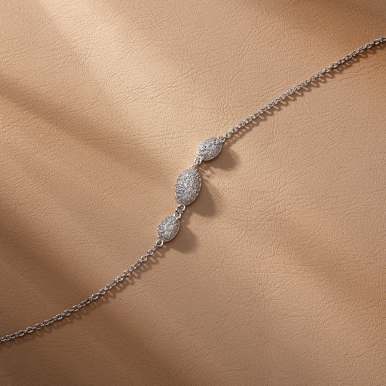 Morellato armband van gerecycled 925 zilver met drie zirkonia-gezette elementen, diagonaal over lichtbruin leer.