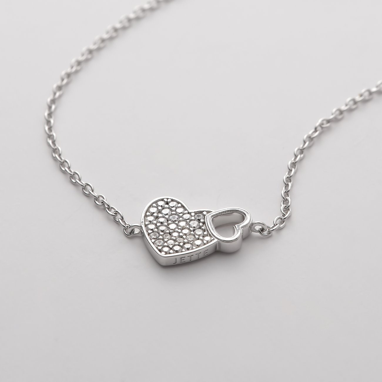 Un bracelet en argent JETTE en argent 925 recyclé avec deux cœurs, l'un pavé de zircone et l'autre ouvert.