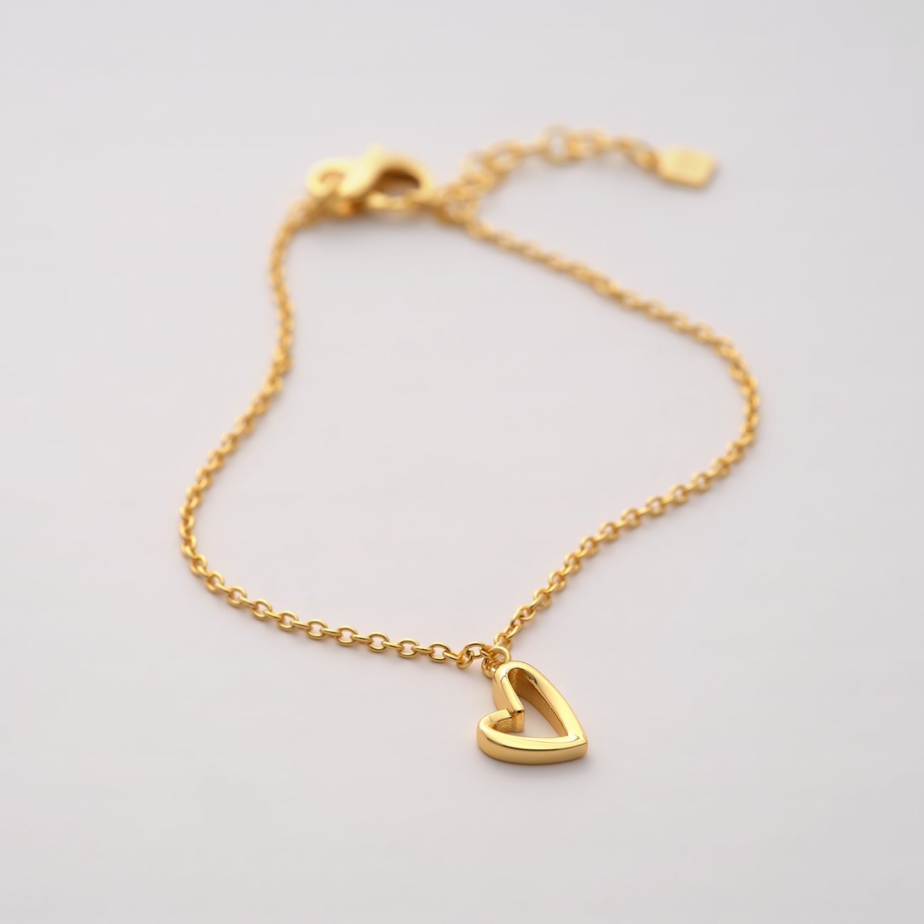 Un bracelet cœur JETTE doré en argent 925 recyclé, affichant un délicat pendentif en forme de cœur.