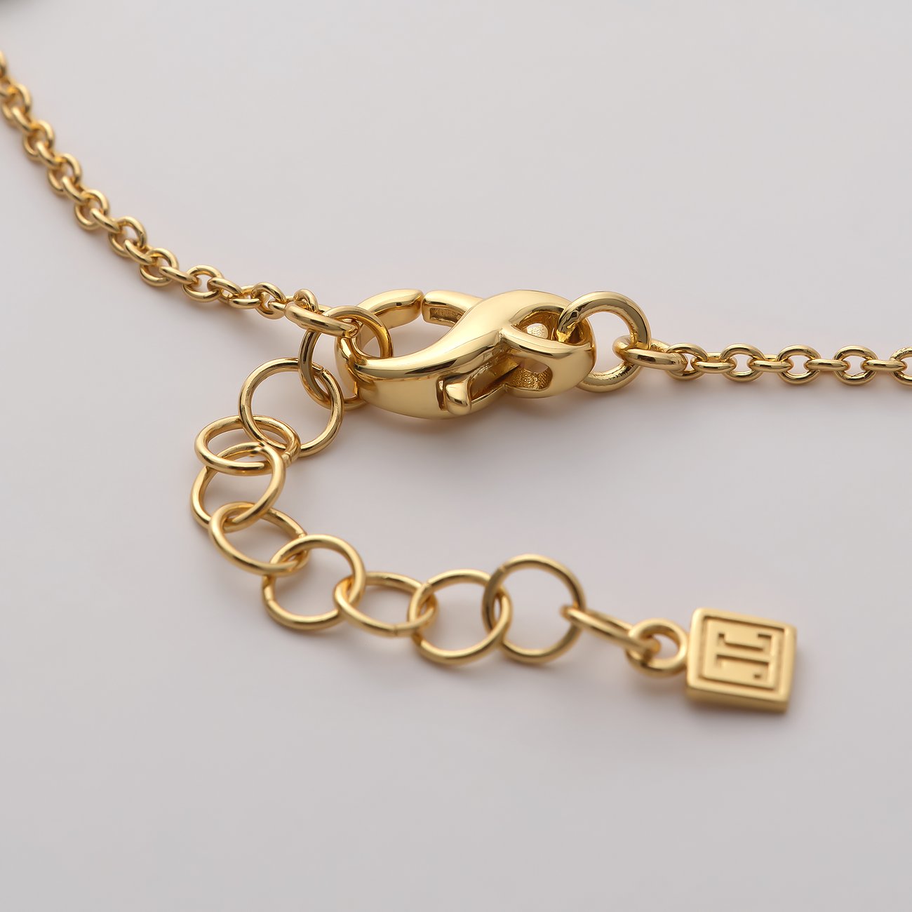 Närbild på låset av ett guldfärgat JETTE armbandsmycke med länk och märkeshänge med logga.