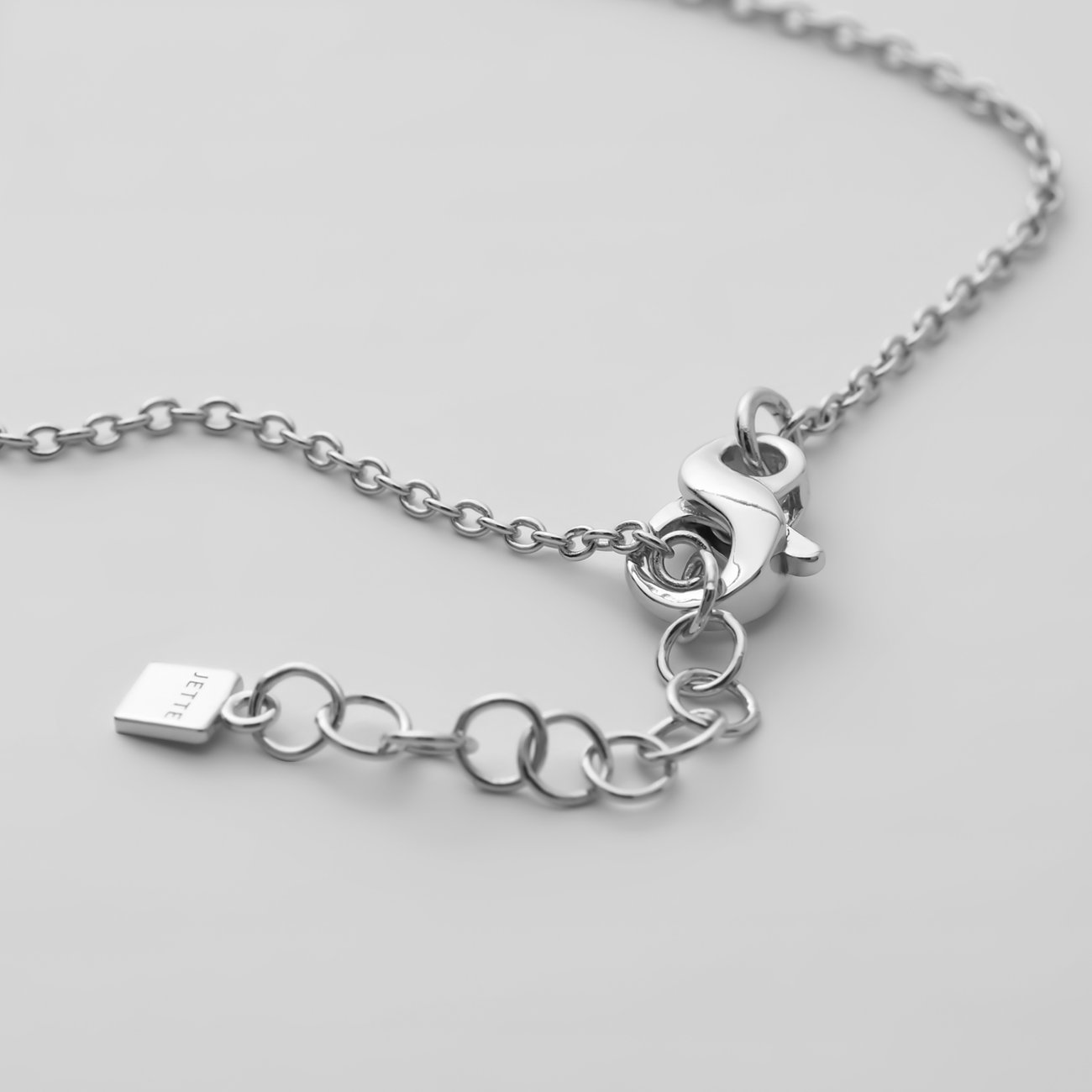 Nahaufnahme des Verschlusses eines JETTE Armschmucks: Karabinerverschluss, Verlängerungskette und Brand-Tag aus recyceltem 925er Silber.